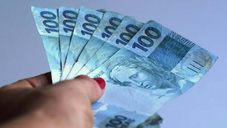 Mulher segurando notas de R$ 100